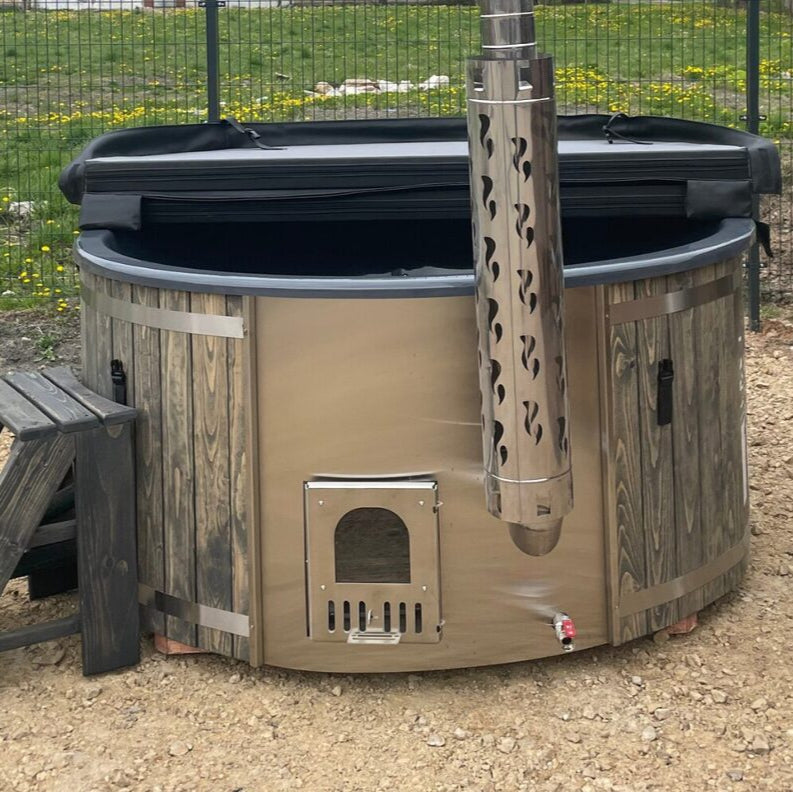 Fiberglass hot tub with integrated wooden heater, surrounded by gravel, with a wooden step leading to its entrance.